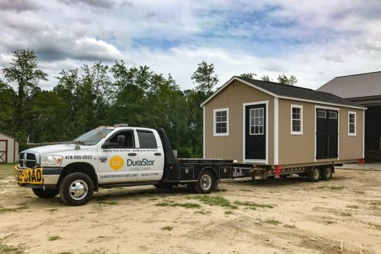 Sheds in - Beige black and white shed being towed to delivery site