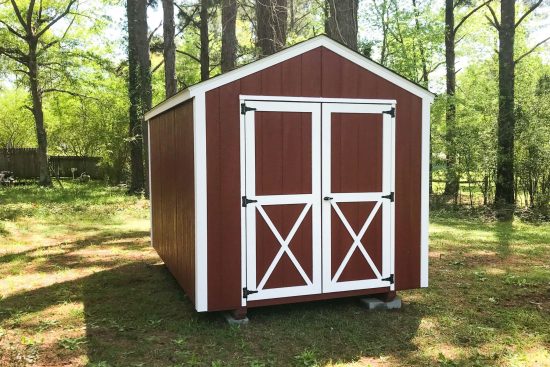 Red utility shed with white trim and white-framed double doors in green forest