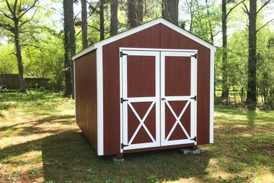 One of our utility sheds in Waycross-red siding with white trimmed double doors and black hinges-set in green wooded area