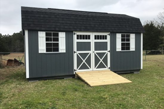 One of our Garden Max sheds in Waycross-gray siding with white trimmed doors and white shutters on windows black roof - Dark trees in background