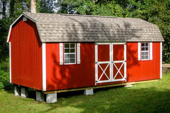 One of our red lofted barn max sheds in Griffin GA - Red siding with white-trimmed double doors and white-framed windows beneath gray roof - set on green grass