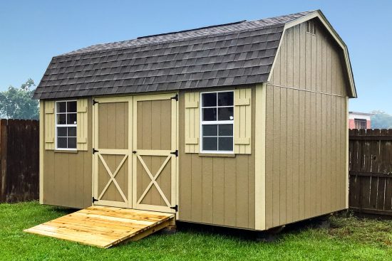 One of our Lofted Barn Max sheds in Douglas GA - Beige siding with cream- colored trimmed double doors and matching window shutters under dark brown shingled roof