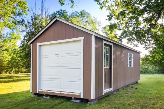 One of our garage sheds in Cordele GA - Brown siding with white overhead and brown side windowed door - white-trimmed side window facing trees