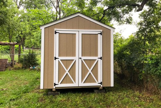 Brown and white utility shed - brown painted wood siding with white-trimmed double doors and corners - shed sits on grassy yard framed with trees