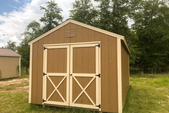 One of our beige and white utility sheds in Athens GA - Brown painted wood siding with off-white trimmed double doors and corners - shed on grassy field with trees in the background