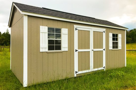 One of our tan Garden Shed Max designs in Athens GA - Beige painted wood siding with white trimmed double doors and corners under shingled dark brown roof - shed in grassy area