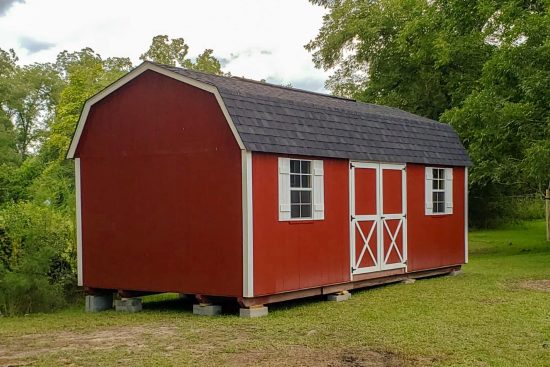 One of our lofted barn max sheds in Athens GA - Red painted wood siding with white trimmed double doors under black shingled roof - shed on grassy area between green trees