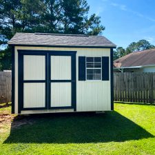 10x12 Garden Shed Max - Navajo white siding with black shingles and trim with matching window shutters - on green grassy fenced yard