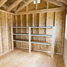 Interior view of 10x12 Garden Shed Max - exposed wood studs, shelves and partial view of rafters in filtered light from window and vent