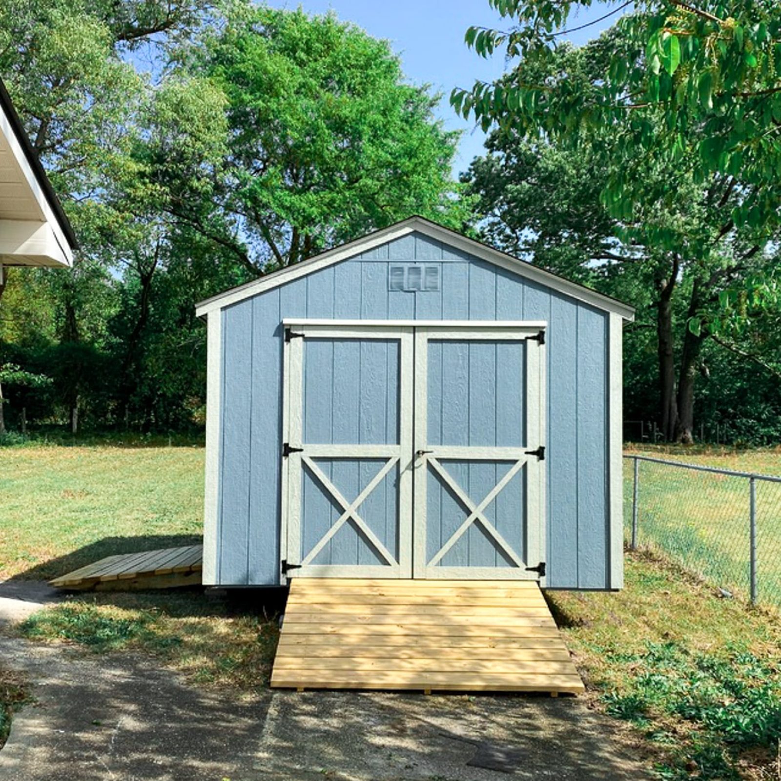 Blue and light silver maple 10x12 Utility Shed in Augusta GA - Blue siding with light silver trimmed double doors with X on lower half - black shingled roof - shed sits on green lawn with green trees in background