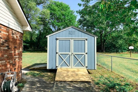 Blue and light silver maple 10x12 Utility Shed in Augusta GA - Blue siding with light silver trimmed double doors with X on lower half - black shingled roof - shed sits on green lawn with green trees in background