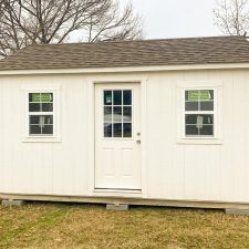 12x16 Utility Shed in Wrightsville GA - White siding and trim with matching window and doors beneath weathered wood shingled roof on client's lawn - bare tree in background