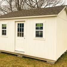 12x16 Utility Shed in Wrightsville GA - White siding and trim with matching window and doors beneath weathered wood shingled roof on client's lawn - bare tree in background