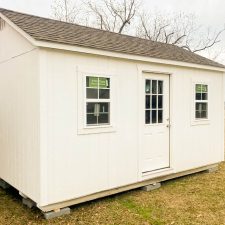 12x16 Utility Shed in Wrightsville GA - White siding and trim with matching window and doors beneath weathered wood shingled roof on client's lawn - bare tree in background