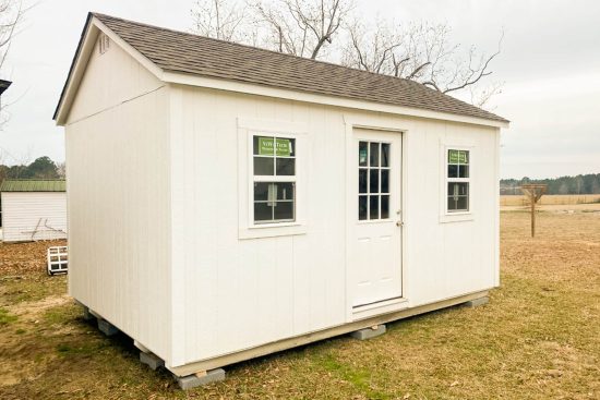 12x16 Utility Shed in Wrightsville GA - White siding and trim with matching window and doors beneath weathered wood shingled roof on client's lawn - bare tree in background