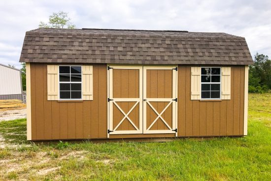 One of our Lofted Barn Max Sheds in McDonough GA - Beige painted siding with off-white trimmed double doors and corners between white-framed windows with matching shutters beneath dark brown shingled roof - Shed sits on green grass under cloudy sky