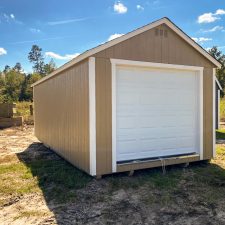 Buckskin and white toned 12x24 garage in Jesup GA - Buckskin colored wood siding with white trim and white overhead doors and matching shutters on lone side window - white-framed window inset buckskin-colored door