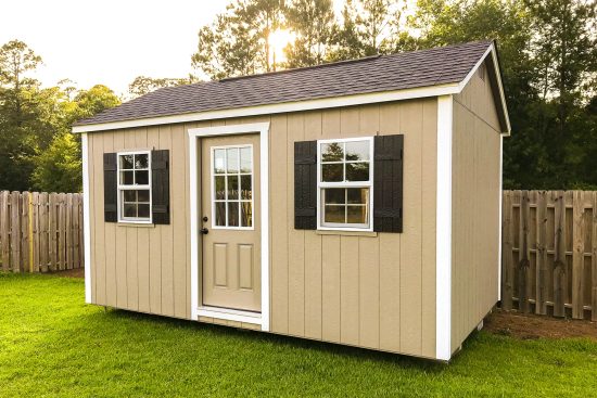 One of our Garden Max sheds in North Augusta SC - Beige painted wood siding with white corner trim - white-framed windows with black shutters flank beige door with window and white door jamb