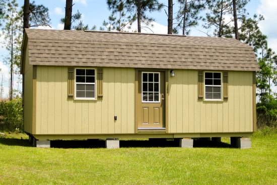 One of our Lofted Shed Max sheds in North Augusta SC - beige painted wood siding with brown door with white-framed window - door flanked by two windows with brown shutters under brown gambrel-style shingled roof