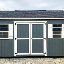 Gray 10x16 Garden Shed Max with white-trimmed double doors on open lot beneath cloudy sky