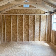 Interior view of a wooden 12x16 Utility Shed with open framing and ample natural light filtering in from window