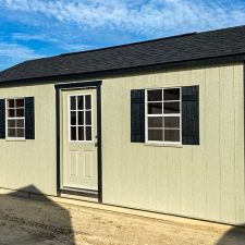 Angled view of beige 12x20 Garden Shed Max with black window shutters and a single entry 9 lite door