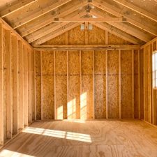 Interior view of 12x20 Garden Shed Max with light filtering through window, highlighting exposed wooden beams, studs and rafters