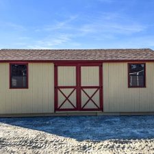 The front view of a 12x24 beige utility shed with red trim and double barn-style doors, with two windows on each side