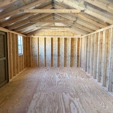 The interior of a 12x24 utility shed, showing exposed wooden framing, spacious open floor plan, and plywood flooring