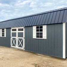 A gray 12x28 lofted barn with a black metal roof, white trim, double barn-style doors, and windows with white shutters, viewed from an angled perspective.