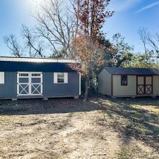 12x28 gray and white Lofted Barn Max beside beige and red 12x24 utility shed among trees