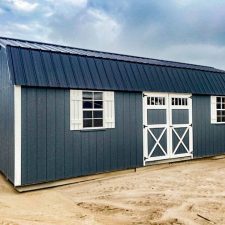 A gray 12x28 lofted barn with a black metal roof, white trim, double barn-style doors, and windows with white shutters, viewed from an angled perspective.