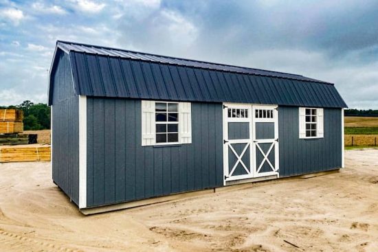 A gray 12x28 lofted barn with a black metal roof, white trim, double barn-style doors, and windows with white shutters, viewed from an angled perspective.