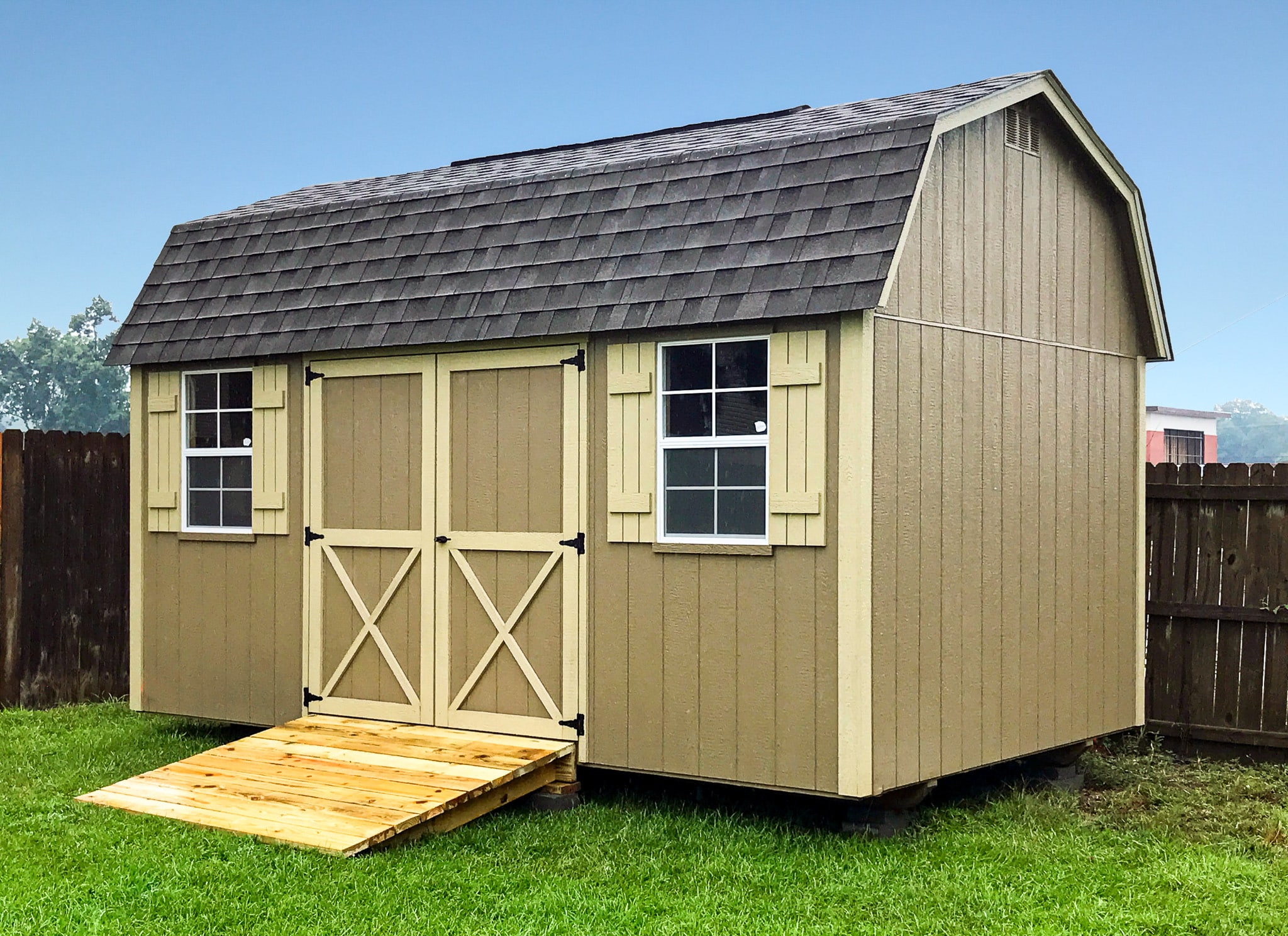 One of our Lofted Barn Max sheds in Douglas GA - Beige siding with cream- colored trimmed double doors and matching window shutters under dark brown shingled roof